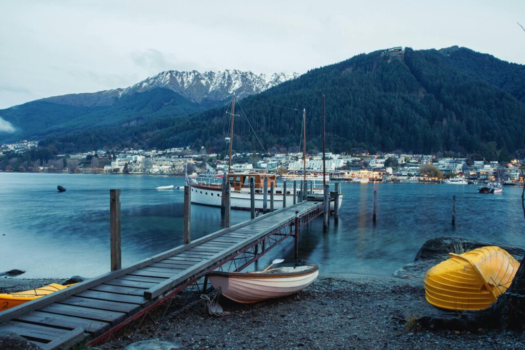 Picturesque view of Queenstown harbor with boats, dock, and mountains.