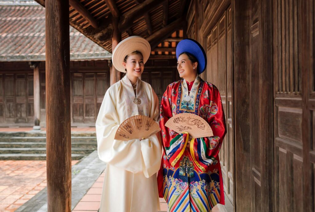 Two women in traditional Vietnamese costumes with fans at a historic temple in Hội An, Vietnam.