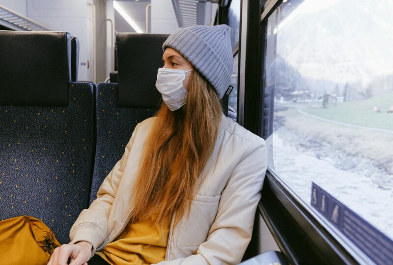 Woman in a train wearing a mask, highlighting travel safety during pandemic.