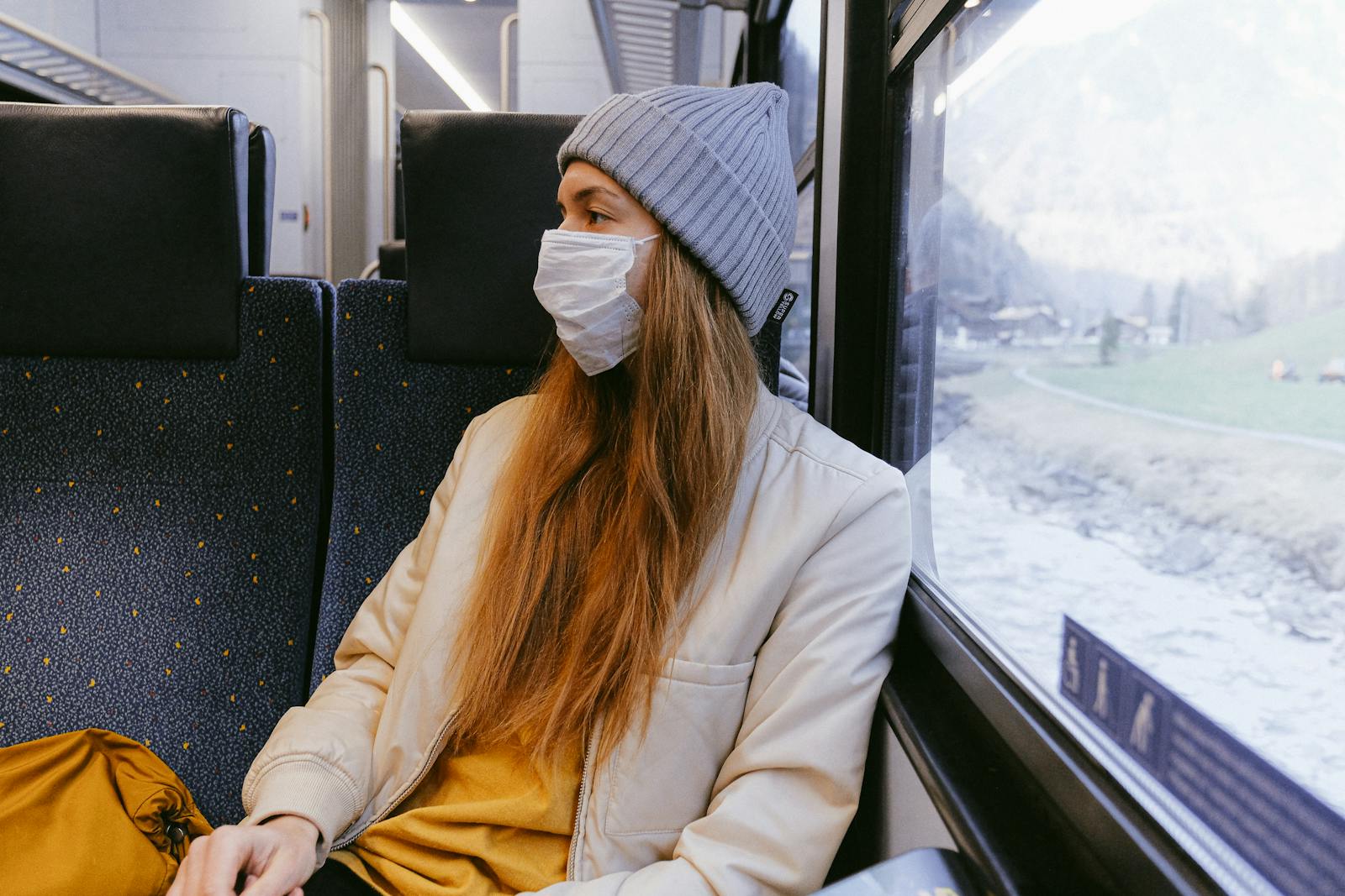 Woman in a train wearing a mask, highlighting travel safety during pandemic.