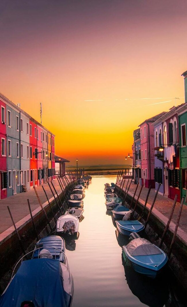 Vibrant facades along Burano's canal with boats at serene sunset. Perfect travel snapshot.