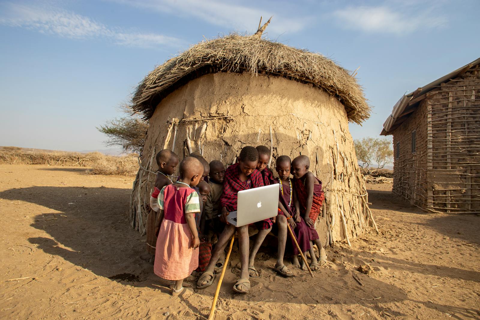 Group of African children in a Tanzanian village using a laptop outdoors, engaged in learning.