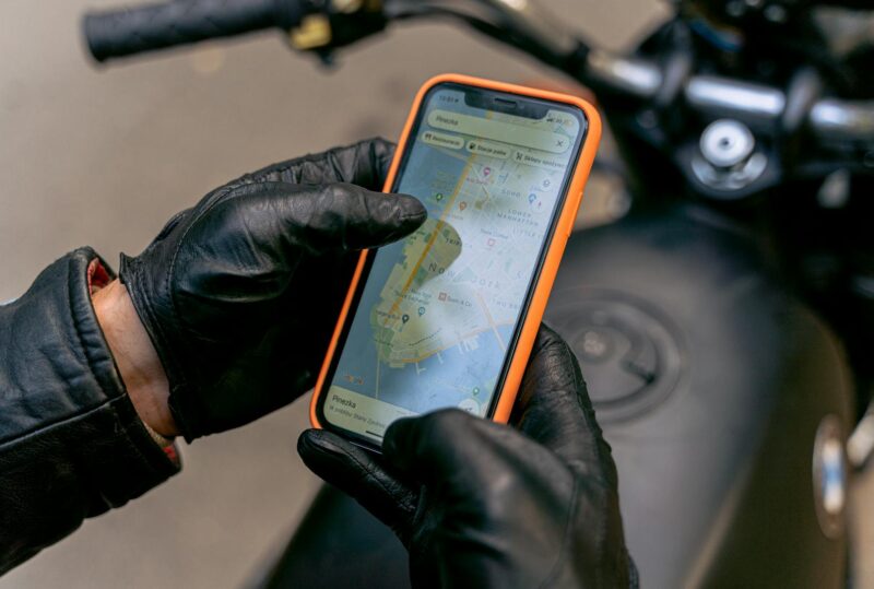 Motorcyclist with gloves using smartphone GPS navigation system while riding.