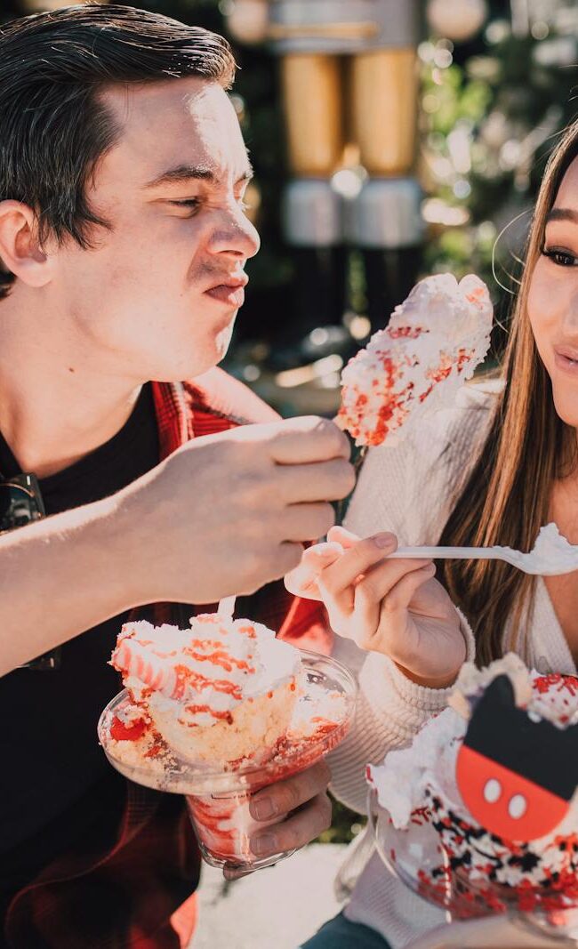 A young couple enjoying colorful desserts on a sunny day outdoors, sharing laughter.