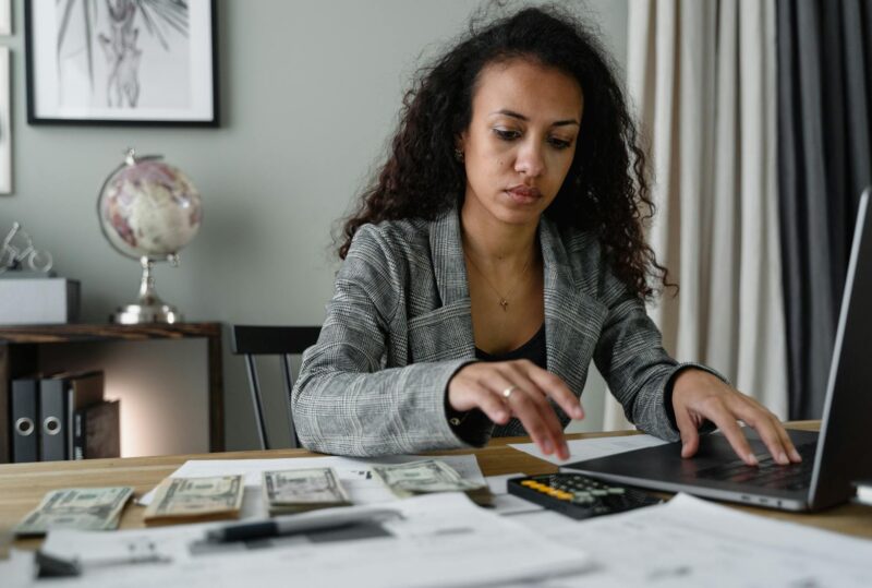 Professional woman analyzing financial documents and counting cash at office desk.