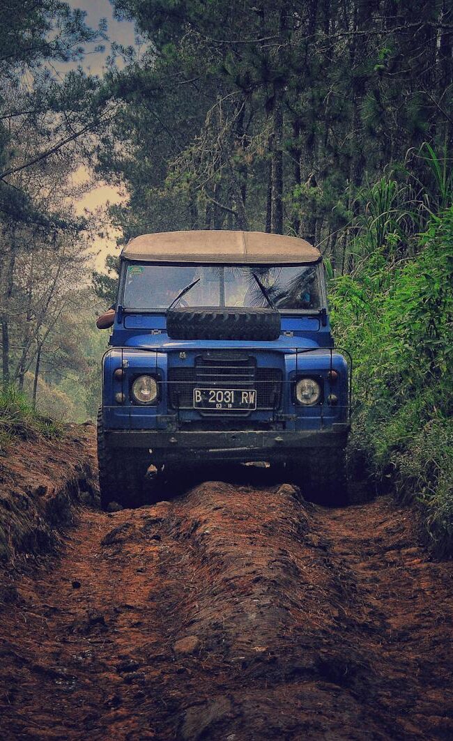 Off-road vehicle traversing a rugged dirt path through lush forest in Parongpong, Indonesia.