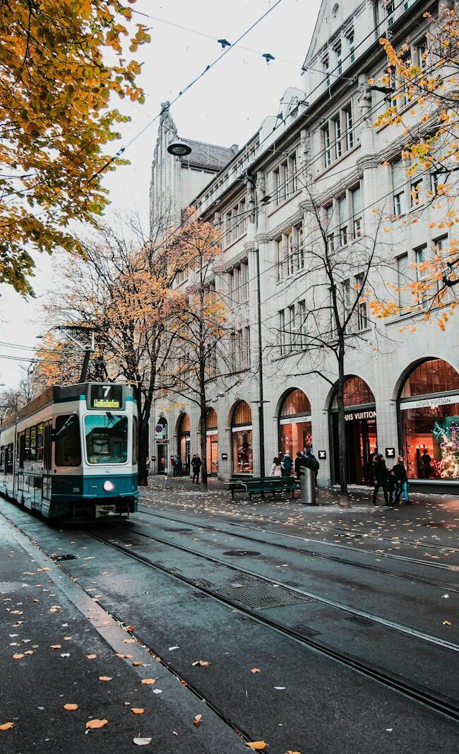 A tram travels down a leaf-strewn street in autumnal Zürich, Switzerland's urban landscape.