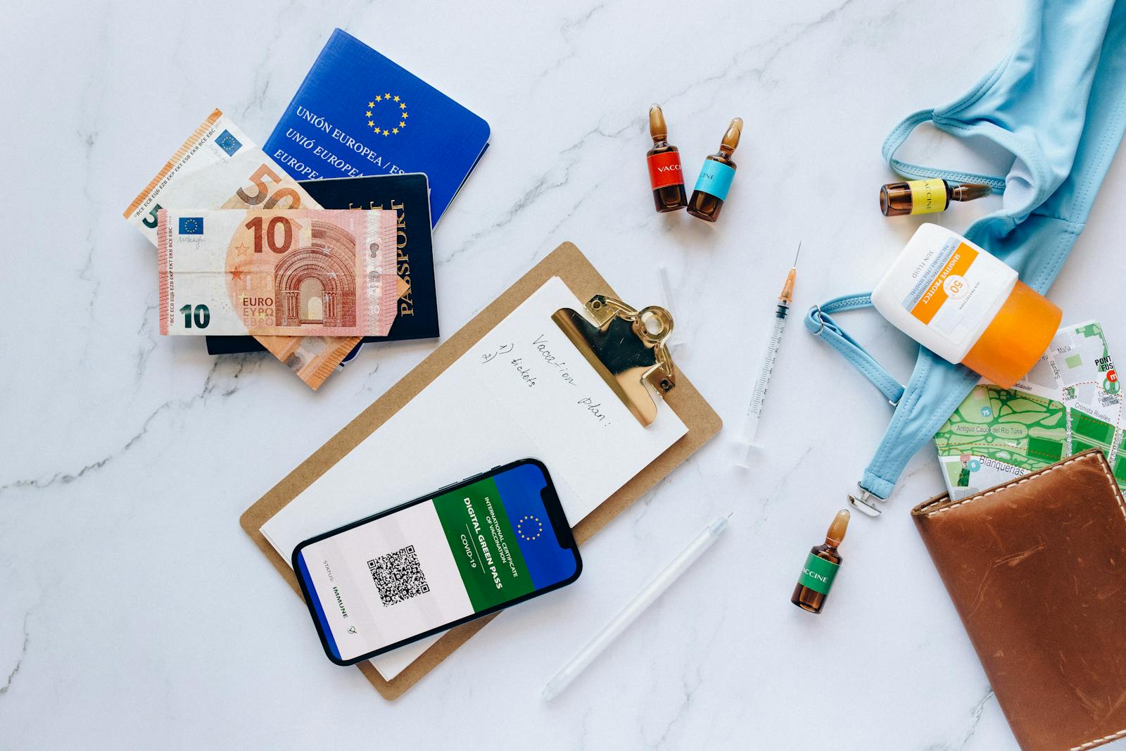 Flat lay of travel essentials including vaccination passport, euros, and medical supplies.