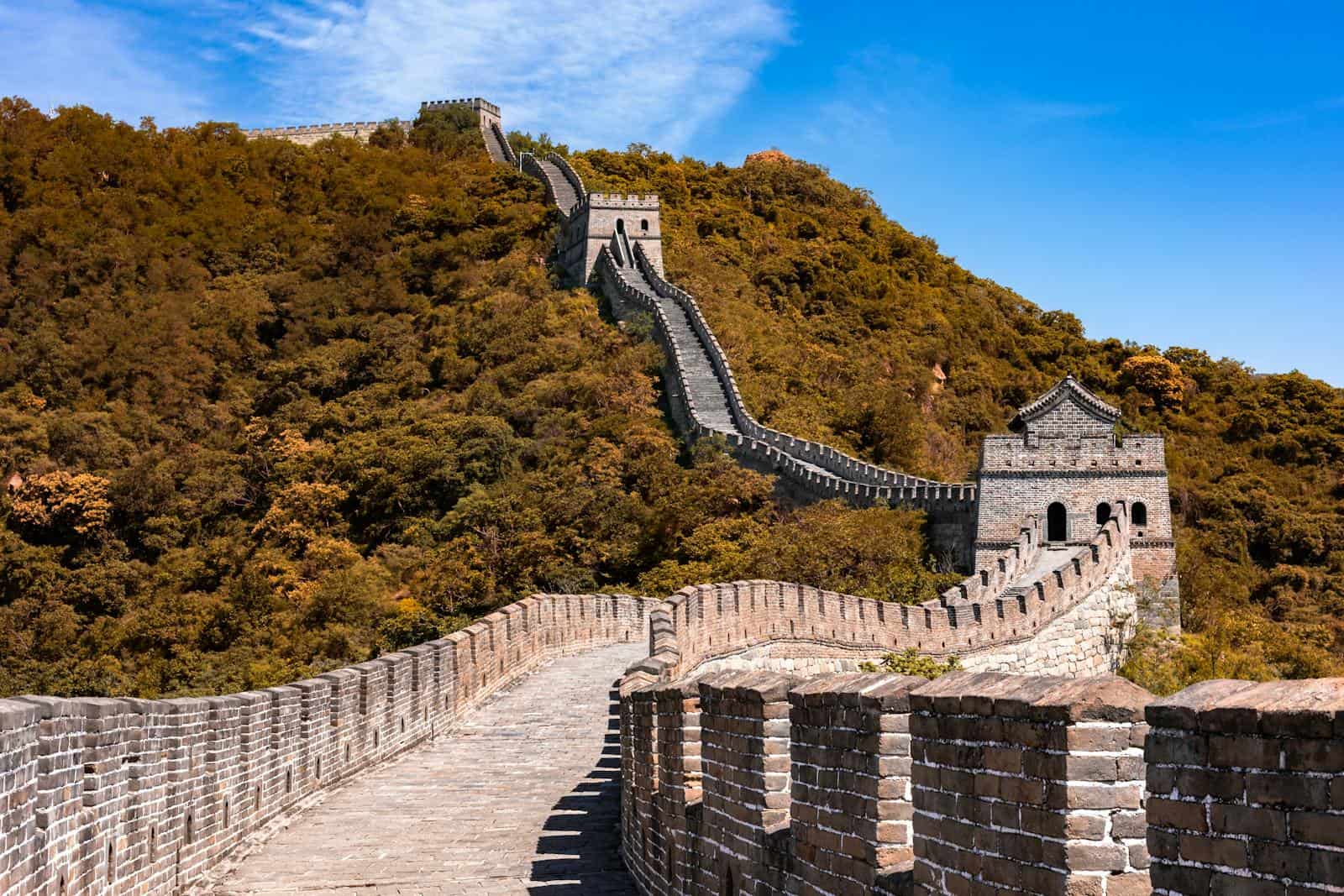 Must see wonders of the world- Majestic view of the Great Wall of China winding through verdant hills under a bright blue sky.