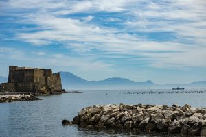 Beautiful view of Castel dell'Ovo by the Bay of Naples with distant mountains and a clear blue sky.