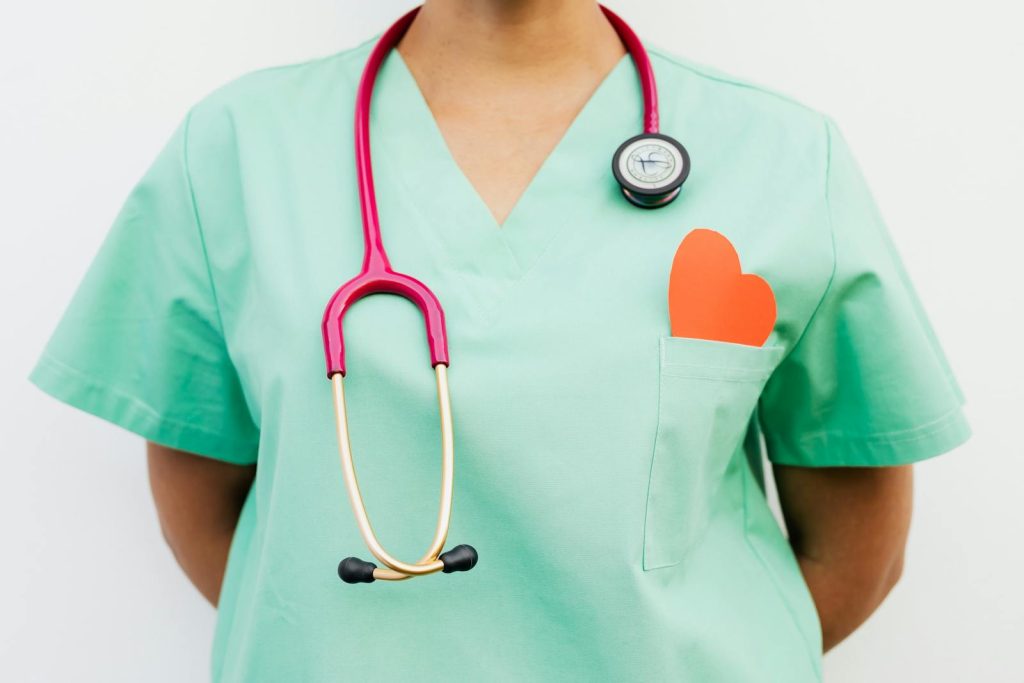 Close-up of a medical professional with a stethoscope and a paper heart cutout on a green uniform pocket.