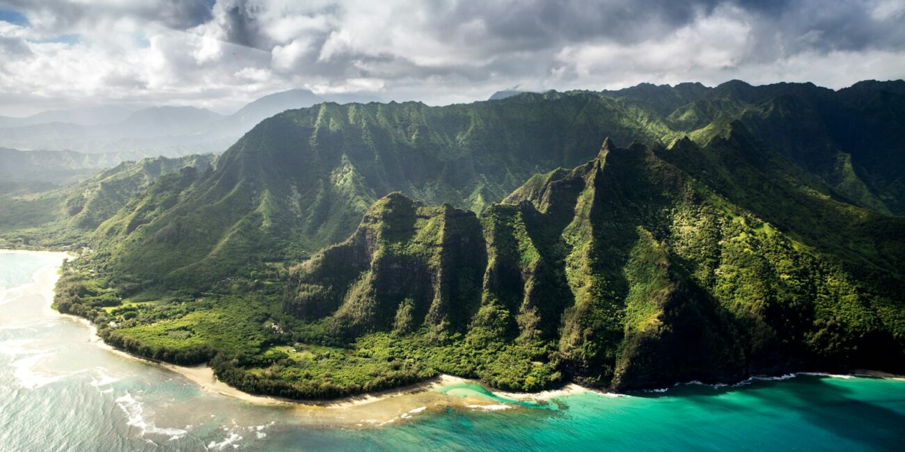 aerial photography of green mountain beside body of water under white sky