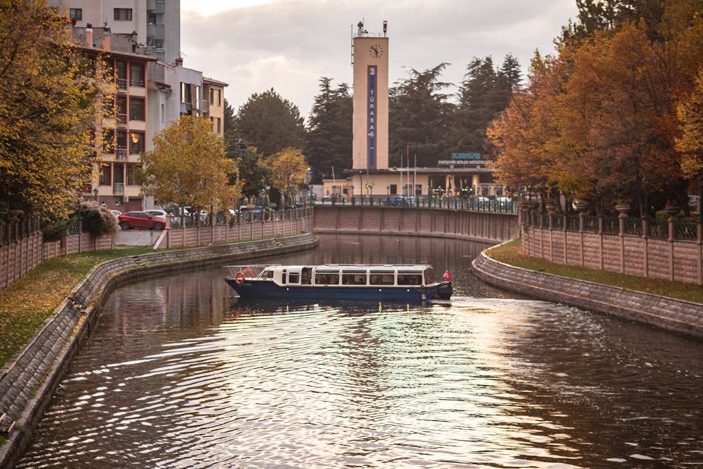 Tour boat gliding through a tranquil canal surrounded by autumn foliage in an urban setting.
