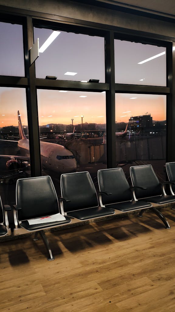 View of empty airport seating area with airplanes outside at sunset.