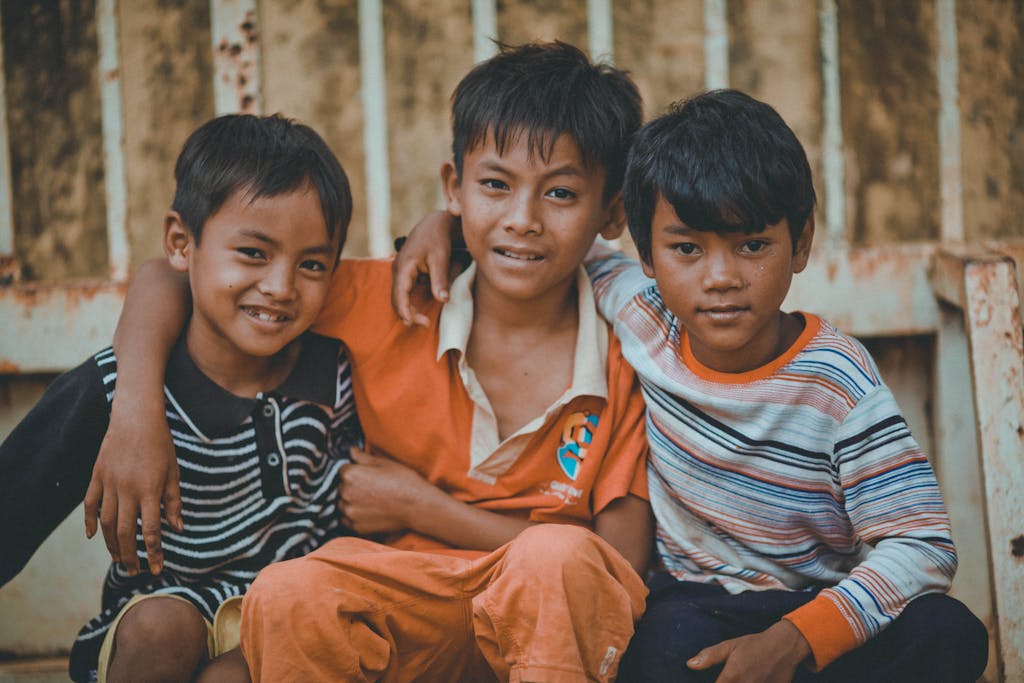Three young boys sitting together and smiling, showcasing friendship and joy, visit Cambodia